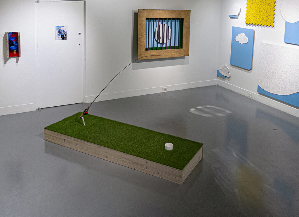 Floor foreground: Quarantine (2021), Fishing pole, PVC pipe, AstroTurf, wood, 60 x 32 x 96 inches; Center back wall: Liberation of the Saint (2021), AstroTurf, paint and mirror on wood 46 x 58 inches